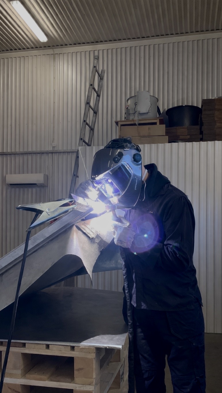 Svetsare i hjälm reparerar metallkonstruktion i verkstad